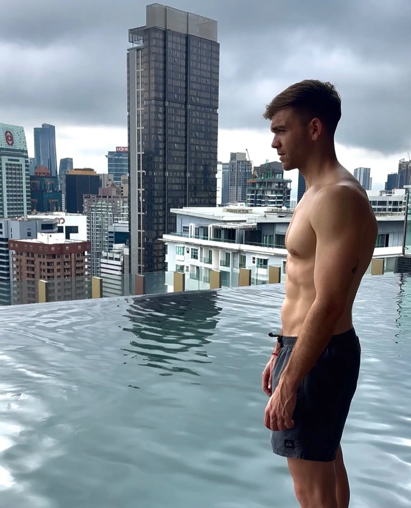 Eneko Andrés de perfil en una piscina infinita sobre un skyline, cielo gris.